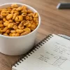 A bowl of puffed wheat on a desk next to a notebook.